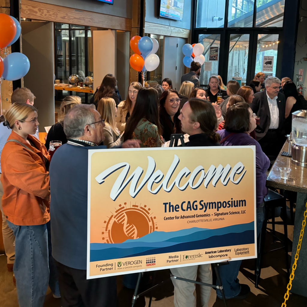 Photo of a social event during the inaugural CAG Symposium in Charlottesville, VA. There is a sign in the foreground headlines "Welcome to The CAG Symposium"